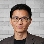 A man in a gray jacket and black shirt stands and smiles