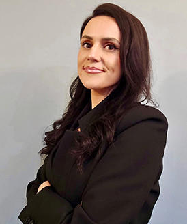 A woman with long dark hair looks at the camera with her arms folded.